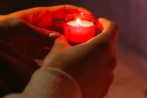Prayer hands holding a small red candle